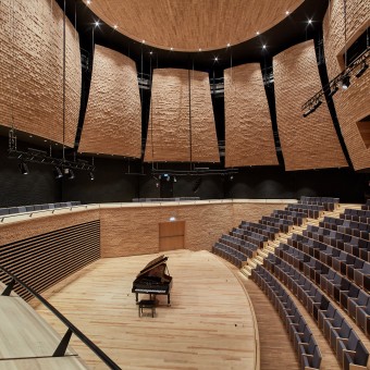 Sala koncertowa z fortepianem na scenie, puste siedziska i drewniane panele akustyczne.